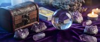 Mystical crystal ball with amethyst stones, wooden treasure chest and candles on purple velvet cloth for spiritual divination and fortune telling practices.