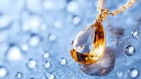 Elegant amber teardrop crystal pendant on gold chain against sparkling water drops and blue background, luxury jewelry macro photography.
