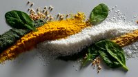 Vibrant yellow turmeric powder and white salt waves with fresh green spinach leaves on dark background, culinary spices composition for food photography and design.