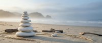 Zen stone stack on sandy beach with driftwood and seashells creating peaceful meditation scene. Balanced rocks symbolize harmony and mindfulness by ocean waves.