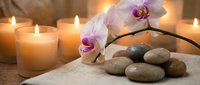 Spa wellness scene with burning candles, pink orchid flowers and smooth massage stones on towel creating peaceful relaxation atmosphere for beauty treatments.