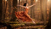 Young woman dancer in flowing orange dress leaping gracefully through autumn forest with golden sunlight and falling leaves creating magical atmosphere.