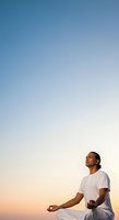 Man of South Asian descent in white casual attire meditating outdoors during golden hour sunset, practicing mindfulness and wellness for relaxation, yoga, and mental health concepts.