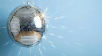 Shiny disco ball with mirror tiles reflecting bright light rays against soft blue background for party and nightclub entertainment events.