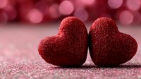 Two red glittery hearts touching on sparkly surface with pink bokeh background for Valentine's Day romance love celebration greeting cards.