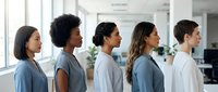 Diverse group of young adults standing in profile inside modern office space with natural light and plants visible in background.