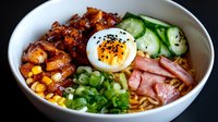 Flavorful ramen bowl with soft-boiled egg, glazed pork belly, corn, cucumber, green onions and noodles in savory broth. Asian cuisine comfort food.