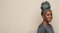 Smiling African American woman with gray braided updo hairstyle wearing dark casual shirt against neutral beige background, portrait.