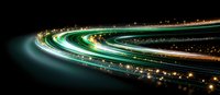Long exposure night photography of curved highway with light trails creating luminous green and orange streaks against dark background, urban transport concept.