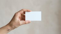 Hand holding blank white business card against neutral background, suitable for branding, corporate identity, and marketing mockup presentations.