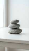 Stacked smooth gray stones balanced on white surface symbolizing zen, meditation, mindfulness, wellness, and tranquility for spa and relaxation design projects.