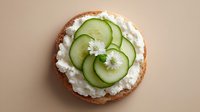 Fresh cucumber slices on creamy cottage cheese spread over toasted bread, garnished with white flowers for healthy breakfast or snack presentation.