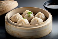 Steamed dumplings with juicy filling in traditional bamboo steamer garnished with fresh herbs, served with dark dipping sauce on black background.