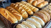 Fresh artisan bread loaves displayed in wicker baskets at bakery showcase with golden crusts and traditional scoring patterns for food service industry.