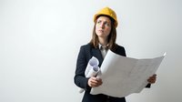 Female architect or engineer with long brown hair and light complexion wearing yellow hard hat and dark business blazer, holding blueprints and construction plans against white background for professional design projects.