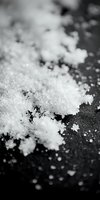 White sea salt crystals scattered on dark surface with shallow depth of field, suitable for food photography, culinary backgrounds, and seasoning product displays.