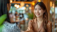 Young Asian businesswoman smiling during meeting in modern cafe. Professional portrait with warm bokeh background perfect for corporate and lifestyle content.