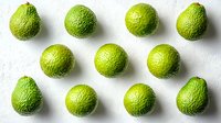 Fresh whole green limes arranged in neat rows on white background, showcasing vibrant citrus texture and natural pattern for food and beverage photography.