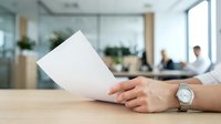 Businesswoman holding blank white paper at desk in modern office with colleagues working in background, suitable for corporate communications and business concepts.