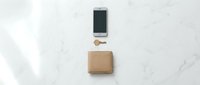 Minimalist flat lay composition with smartphone, kraft paper package and wooden spoon on white marble surface for modern lifestyle branding.