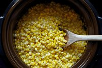 Golden corn kernels cooking in slow cooker with wooden spoon for healthy meal preparation and comfort food recipes.