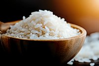 Steamed white rice grains in wooden bowl against dark background, close-up macro shot with selective focus and warm lighting for food photography.