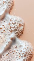 White foam bubbles and soap suds on peach colored background with water droplets creating abstract texture pattern for cosmetic and skincare advertising.