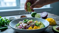 Hand squeezing fresh lime juice over vibrant salad bowl with vegetables, herbs and mango. Food preparation and healthy eating concept for culinary and nutrition content.