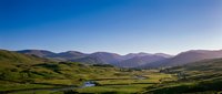 Scenic mountain valley landscape with rolling green hills, winding river, and distant peaks under clear blue sky, suitable for travel and nature backgrounds.