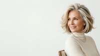 Mature woman with shoulder-length blonde wavy hair, fair complexion, wearing cream turtleneck sweater, smiling at camera against white background for portrait and lifestyle use.