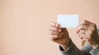 Senior man with dark skin holding blank white card against neutral beige background, suitable for business messaging, greeting cards, and promotional campaigns.