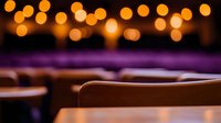 Blurred golden bokeh lights create dreamy atmosphere above empty wooden chairs in dark room, soft focus background adds romantic mood for event space design.