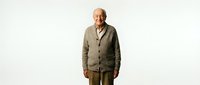 Senior man with light skin tone wearing casual beige cardigan and olive pants, standing against white background. Suitable for lifestyle, healthcare, retirement and family-related projects.