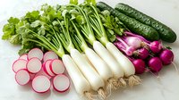 Fresh spring vegetables arranged on white background including sliced radishes, white daikon radish, red onions, cucumbers and parsley. Clean eating and healthy food concept.