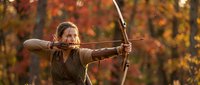 Young woman archer drawing wooden bow in autumn forest with golden foliage background. Traditional archery sport and outdoor recreation concept.