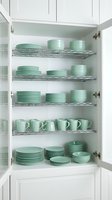 Organized kitchen cabinet with mint green dinnerware set including plates, bowls and mugs neatly arranged on wire shelving for home storage solutions.