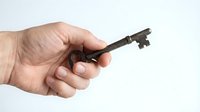 Hand holding vintage rusty metal key on white background, isolated object for security, access, unlock, antique, mystery, real estate concepts.