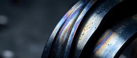 Metallic rings with rainbow iridescent surface and water droplets creating prismatic light effects on dark background for modern design projects.