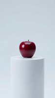 Fresh red apple on white cylindrical pedestal against light gray background for minimalist product photography and healthy lifestyle concepts.