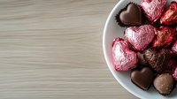 Heart-shaped chocolates and wrapped candies in white bowl on wooden surface for Valentine's Day celebration and romantic occasions.