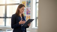 Professional businesswoman using digital tablet in modern office environment with natural lighting and colorful wall displays.