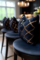 Luxurious navy blue velvet barstools with decorative gold geometric pattern cushions create elegant seating in modern restaurant interior with ambient lighting.