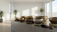 Singing bowls and mallets arranged on marble platform in bright minimalist interior with potted plants and natural light for wellness and meditation.