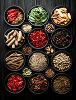 Assorted traditional Chinese medicine ingredients and dried herbs in black ceramic bowls on dark wooden background, overhead view of natural healing elements.