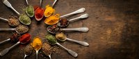 Colorful spices and herbs arranged in wooden spoons on rustic table, perfect for culinary designs, cooking blogs, restaurant menus, and food packaging.