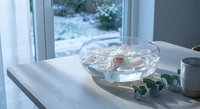 Elegant glass bowl with floating pink roses and candles on wooden table near window creating romantic spa-like atmosphere for relaxation and wellness.