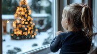 Young blonde girl looking through window at illuminated Christmas tree outside during snowy winter evening, creating nostalgic holiday atmosphere.