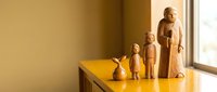 Wooden family figurines arranged by size on yellow surface near window creating warm minimalist home decor display with natural lighting and cozy atmosphere.