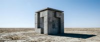 Abandoned concrete bunker structure standing alone in vast desert landscape under clear blue sky, suitable for editorial, architectural, and conceptual projects.