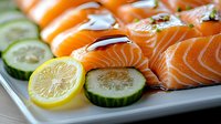 Fresh raw salmon sushi pieces arranged on white plate with sliced cucumber and lemon garnish, showcasing vibrant orange fish texture and healthy ingredients.